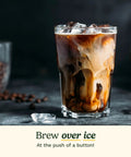 Glass of iced coffee with swirling milk beside scattered coffee beans and ice cubes, promoting over ice brewing feature.