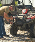 Man installing ATV Seeder With 125 Lb Hopper And Universal Mounting System on red ATV for seeding and land management