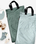 Two Reusable Hanging Wet Dry Bag Duo For Baby Gear And Travel Needs with black handles, surrounded by baby items.