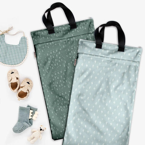 Two Reusable Hanging Wet Dry Bag Duo For Baby Gear And Travel Needs with black handles, surrounded by baby items.