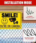 Two Pack Smile Youre On Camera Signs 10 By 7 Inch Funny Security Signs With Smile Face And Camera Icon Rust Free Aluminum UV Printed And Weatherproof Surveillance Signs For Business Home And Office mounted on fence with installation instructions