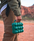 Person carrying Tough 12-Egg Plastic Carrier With Locking Lid, Molded Handle, And Secure Fit For Camping in outdoor setting