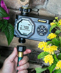 Hydrologic 4 Zone Digital Water Timer With Smart Zone Control attached to hose among garden flowers