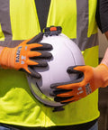 Person wearing Rugged Knit Dipped Work Gloves With Nitrile Coating For Cut Resistance ANSI A1 holding a white helmet