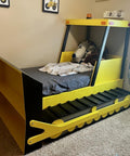Front view of a kids' bulldozer-style bed: yellow frame, black track base, front blade, stuffed animals in cab.