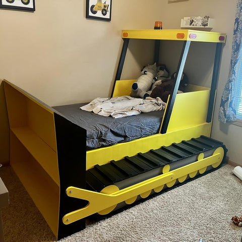 Front view of a kids' bulldozer-style bed: yellow frame, black track base, front blade, stuffed animals in cab.