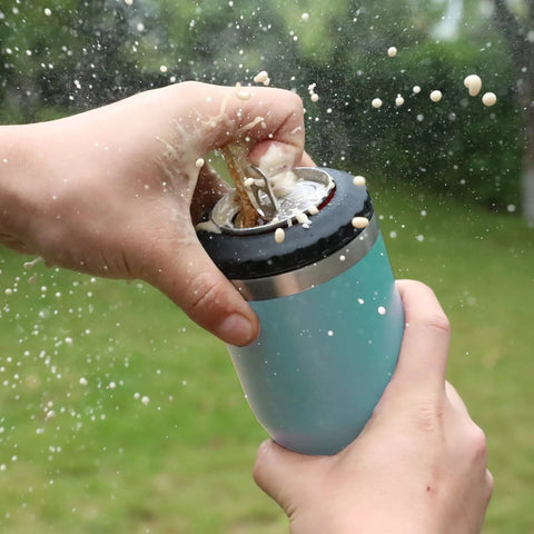 Hands holding 4 In 1 Insulated Stainless Steel Can Insulator That Fits Standard And Slim 12 Oz Cans And Beer Bottles Doubles As A 12 Oz Insulated Tumbler For Outdoor Adventures, lake blue, with beer spraying outdoors.