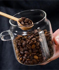 Go Ahead And Upgrade Your Countertop Setup With This Solid Clear Glass Storage Jar Featuring An Airtight Sealed Kitchen Canister And Wooden Spoon For Coffee Beans 900Ml Capacity Handles Dry Goods Smoothly And Looks Dope. Image shows a glass jar filled with coffee beans and a wooden spoon.