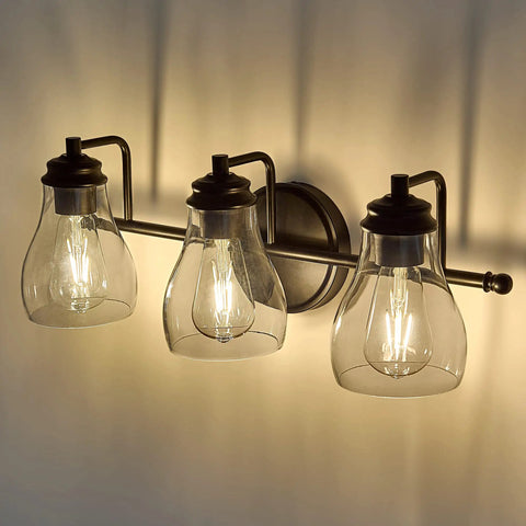 Black Three Light Vanity Light Fixture With Clear Glass Shades For Bathroom Over Mirror, warm glow on wall