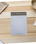 White Poly Mailer Bags 100 Pack 10x14 Inch Waterproof Self Seal Envelopes on a wooden table