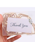 Hand holding pack of 16 gold heart carabiner clips in transparent box with 'Thank You' note, Gold Heart Carabiner Clips 16 Pack For Backpacks And Hiking Gear