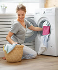Woman placing a peach pink flannel heating pad replacement cover into a washing machine for cleaning.