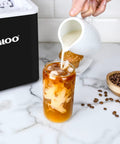 Person pouring milk into iced coffee next to Portable Countertop Ice Maker With Self Cleaning Produces 26 Lbs A Day Ice Ready In 6 To 8 Minutes Includes Ice Scoop And Basket Compact Desktop Unit For Home Office Or Parties