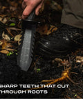 Hand holding Beefy Heavy Duty Metal Detecting Shovel With Double Serrated Blade cutting through roots in soil.