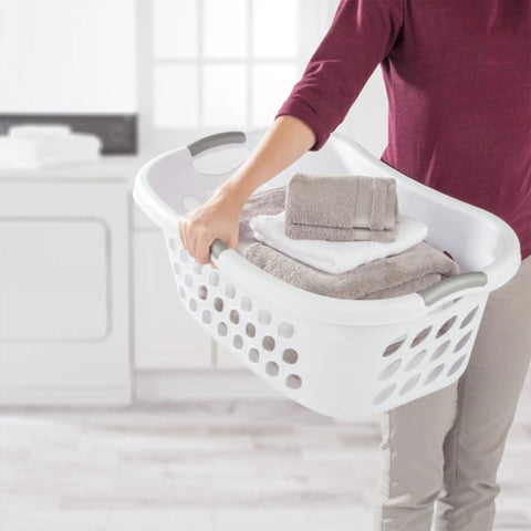 Person carrying a Six Pack HipHold Laundry Basket 1.25 Bushel White Contoured Plastic Hamper With Ventilated Holes And Comfort Grip Handles.