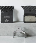 L05A Brake Pads In ACE Ultegra Hard Resin For Road Bikes, Multicolor Set displayed on concrete surface with metal holder