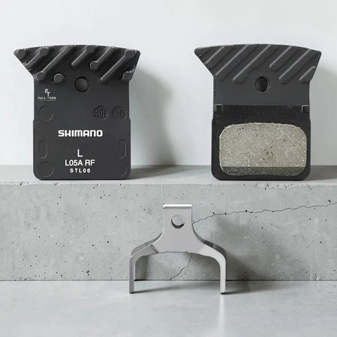 L05A Brake Pads In ACE Ultegra Hard Resin For Road Bikes, Multicolor Set displayed on concrete surface with metal holder