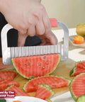 Side view of JAYVAR extra-large crinkle cutter with pink handle slicing watermelon on a cutting board