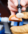 Dremel rotary tool with white polishing wheel shaping an orange curved wooden piece