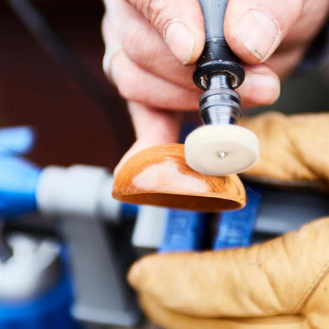 Dremel rotary tool with white polishing wheel shaping an orange curved wooden piece