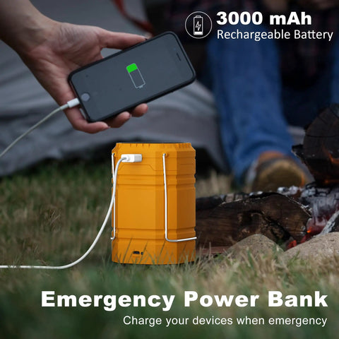 Person charging phone with Go-To LED Camping Lantern With USB Rechargeable, Solar Panel And Hand Crank, next to a campfire.