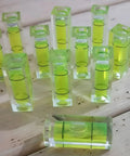 6Pcs Small Bubble Level 10x10x29mm Mini Square Spirit Level Picture showing multiple green bubble levels on wooden surface.