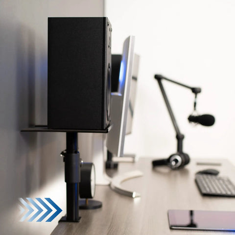 Clamp-On Speaker Stand Desk Mount Set Two-Pack With Adjustable Height And Tilt Universal 9.5x8.8 Platforms For Computer And Bookshelf Speakers EVA Padding Cuts Vibration Heavy-Duty Black holding speaker on desk next to computer monitor.