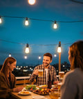 Friends enjoying a meal under 100Ft Solar String Lights Outdoor Waterproof With Remote Dimmer Lit Backyard Vibes 32 Vintage Edison Bulbs