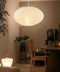 FEHEED 16 Inch Oval Plug in Hanging Paper Lantern Lights with Cord illuminating a modern dining area, surrounded by plants.