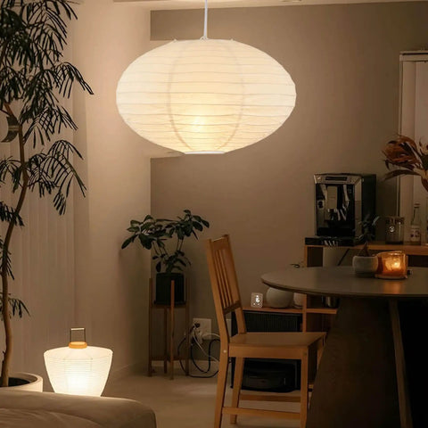 FEHEED 16 Inch Oval Plug in Hanging Paper Lantern Lights with Cord illuminating a modern dining area, surrounded by plants.