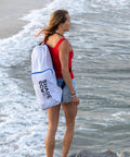 Person carrying Easy Setup Beach Canopy Tent 8.5x9 Ft UPF50 Plus Sun Shade Portable Four Post Shelter on a beach in white carry bag.