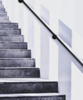 Heavy Duty 7 Ft Metal Industrial Pipe Stair Handrail In Glossy Black Finish mounted on indoor concrete stairs.
