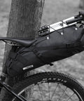 Black waterproof bike saddle bag with expandable 10L and 13L capacity, attached under seat on bicycle for mountain road biking.