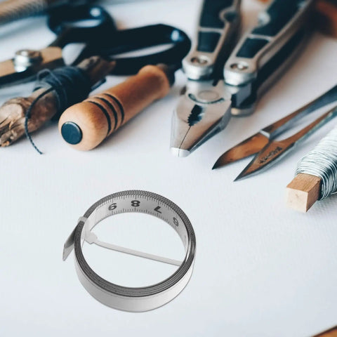No Fuss Self Adhesive One Meter Steel Metric Track Ruler Tape on a white surface with tools, showing its laid flat design.