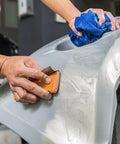 Hand using Pro-Grade 1000 Grit Wet Or Dry Sandpaper Sheets 5-1/2 X 9 In Box Of 25 for sanding car surface in auto body shop.