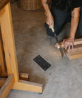 Person sawing wood near Beefy Heavy Duty Flat Plate Corner Brackets With Screws Black 10x5cm Set For Tables and Chairs on floor