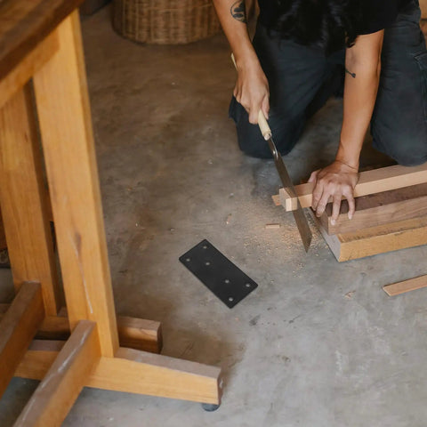 Person sawing wood near Beefy Heavy Duty Flat Plate Corner Brackets With Screws Black 10x5cm Set For Tables and Chairs on floor