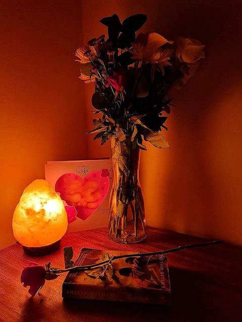 Himalayan Pink Salt Lamp With Dimmable Warm Glow Handcrafted Wooden Base beside flowers on a wooden table creating a cozy vibe