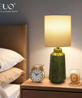 Green Ceramic Table Lamp With Leaf Pattern And White Linen Shade, 17 Inch Tall on bedside table with clock and candle.