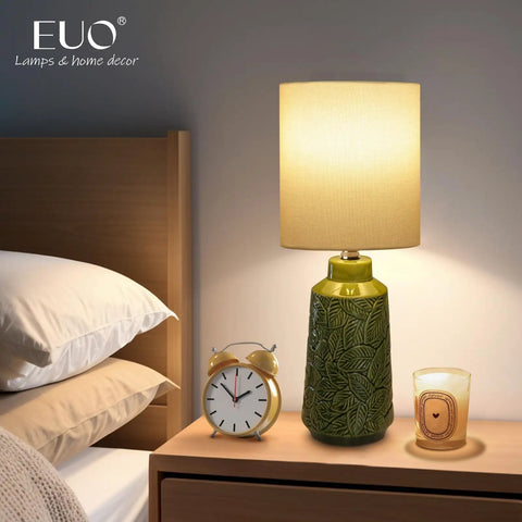 Green Ceramic Table Lamp With Leaf Pattern And White Linen Shade, 17 Inch Tall on bedside table with clock and candle.