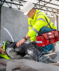 MFASCO emergency first aid trauma bag, red with reflective straps, carried by a safety responder treating a worker.