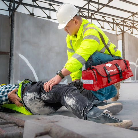 MFASCO emergency first aid trauma bag, red with reflective straps, carried by a safety responder treating a worker.