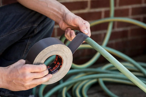 Applying Ferociously Strong Duct Tape One Point Eight Eight Inch By Thirty Five Yard Dark Gunmetal Gray to hose for outdoor repair
