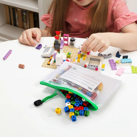 Child assembling blocks next to a 30 Pack Small Zipper Mesh Pouches With Label Pockets, A6 Size 6.3 By 4.7 Inches, in use for toys.