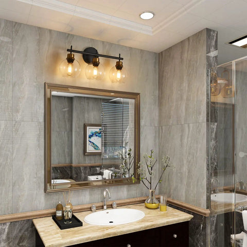 Three Light Black And Gold Bathroom Vanity Light Fixture With Metal Base And Clear Glass Globe Shades, Modern Over Mirror Bath Lighting That Elevates Your Space With Sleek Durable Build And High End Look in elegant bathroom setting.