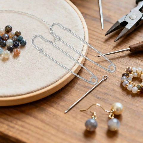 Heavy Duty Safety Pins Set For Clothes And Shawls on a wood table with beads and crafting tools.