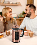 Couple enjoying drinks with 34 Ounce French Press Coffee Maker With Heat Resistant Borosilicate Glass, Stainless Steel Frame on table.