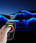 Hand using RGB LED Dimmer Switch with RF Wireless Control and Sliding Remote, illuminated house with LED strip lights, night scene.
