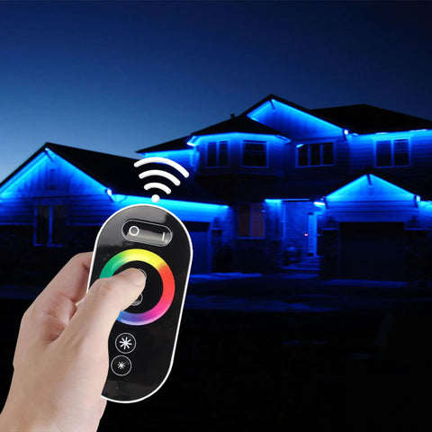 Hand using RGB LED Dimmer Switch with RF Wireless Control and Sliding Remote, illuminated house with LED strip lights, night scene.
