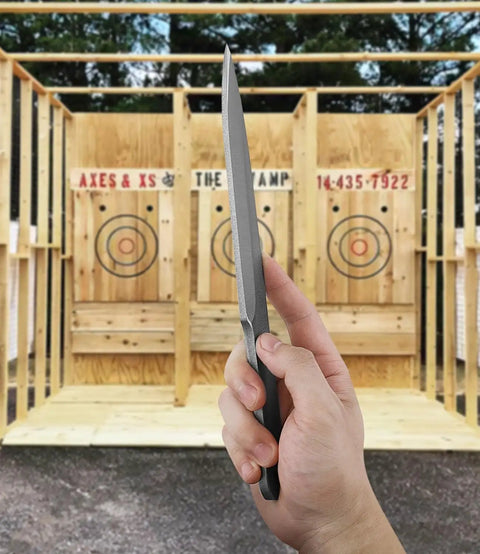 Hand holding spear from 10.2 Inch Throwing Spear Set, 0.236 Inch Thick Full Tang at target range, showing nylon sheath, six pack for competition.